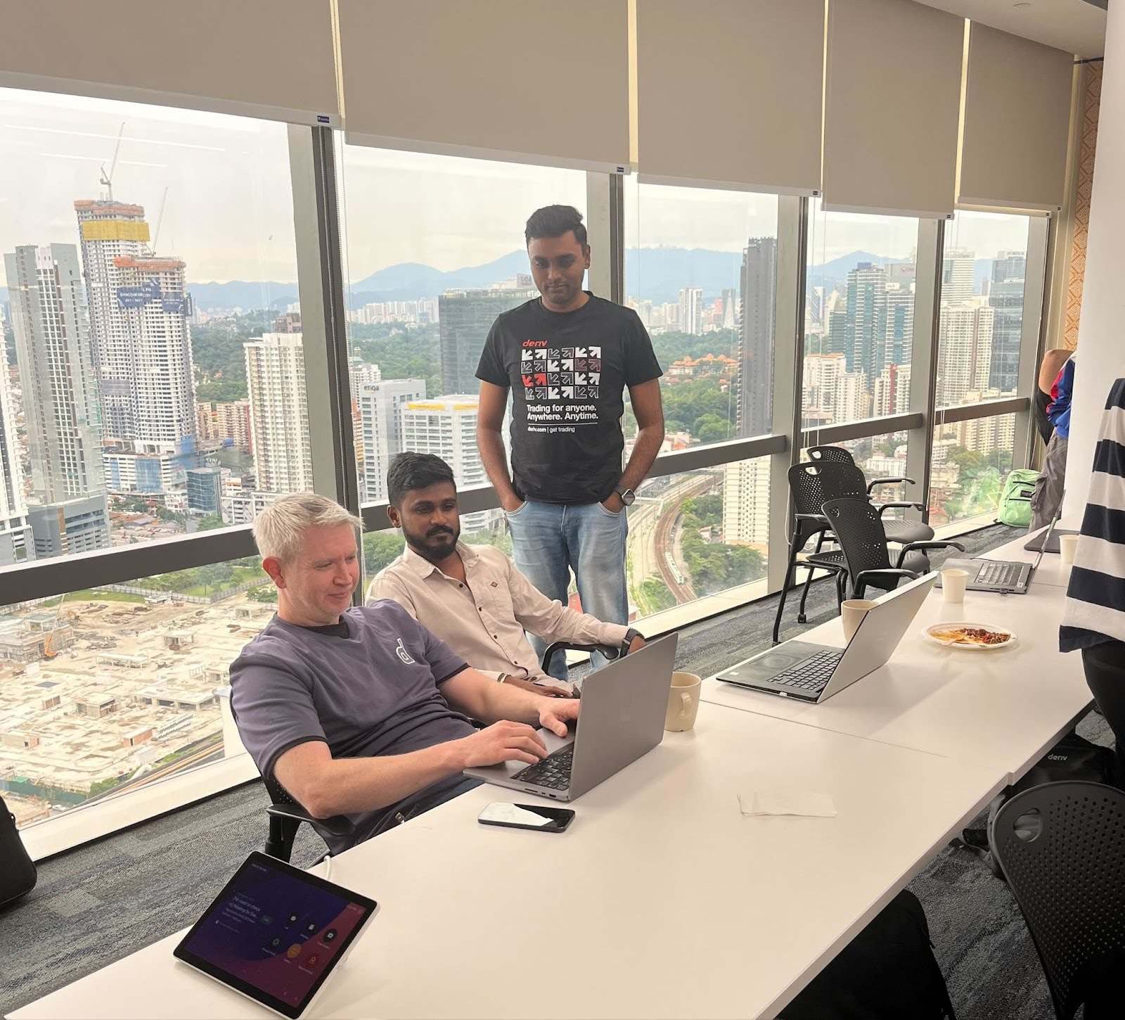 David Usher, Deriv’s VP of Engineering sitting with colleagues and working on a laptop